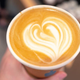 Hand holding latte with heart-shaped milk froth on top